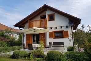 Een tweelaags huis met een balkon, een terras met stoelen en een parasol, en een schotelantenne.