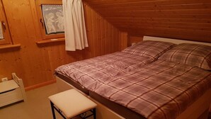 Ett sovrum med en säng, en bänk, ett fönster med gardiner och träväggar.