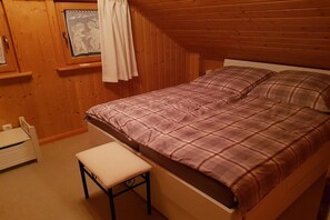 Een slaapkamer met een bed, een bankje, een raam met gordijnen en houten wanden.