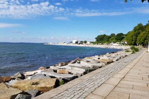 Eine Uferpromenade mit einem Steinweg, felsigem Ufer und Gebäuden in der Ferne.