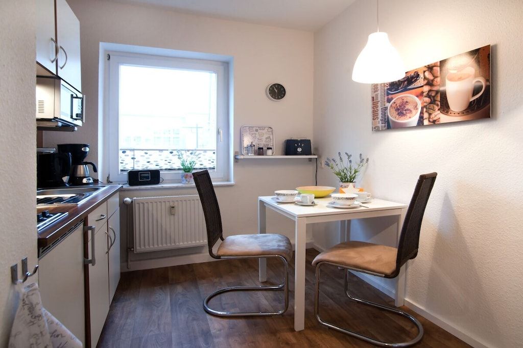 Une cuisine de taille réduite avec une fenêtre, une table à manger avec des chaises et une horloge fixée au mur.