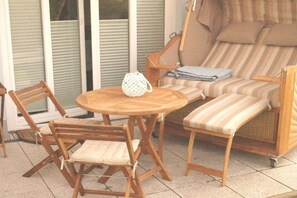 Un espacio al aire libre con una mesa redonda de madera, dos sillas de madera, un sofá a rayas y una lámpara blanca pequeña.