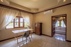 A room with a wooden desk, a patterned chair, a tall cabinet, and a sofa in a corner. - Giant Palm Tree Views Retreat. Castle-Style Private Pool Villa. (Chalong)