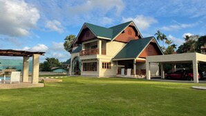 A two-story house with a green roof, a balcony, and a covered patio area. - Giant Palm Tree Views Retreat. Castle-Style Private Pool Villa. (Chalong)