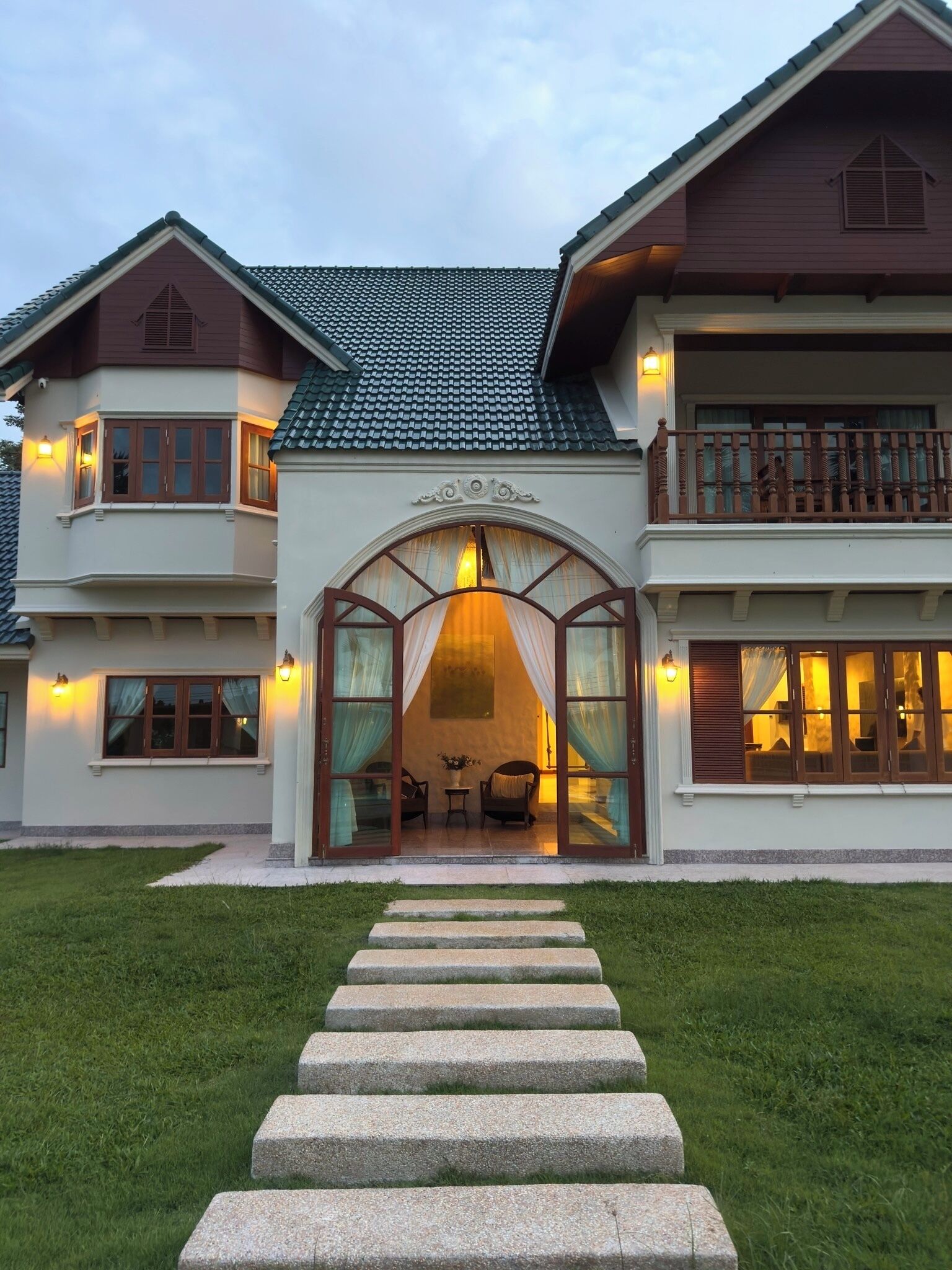 Une maison à deux étages avec une entrée centrale, un balcon à l’étage supérieur et une pelouse bien entretenue.