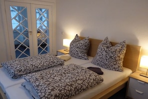 A hotel room with a bed, two bedside lamps, a nightstand, and a door with glass panels. - Holiday apartment with 1 bedroom (Ribnitz-Damgarten)