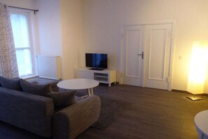 A living room with a sofa, a small table, a television on a stand, and a door. - Holiday apartment with 1 bedroom (Ribnitz-Damgarten)