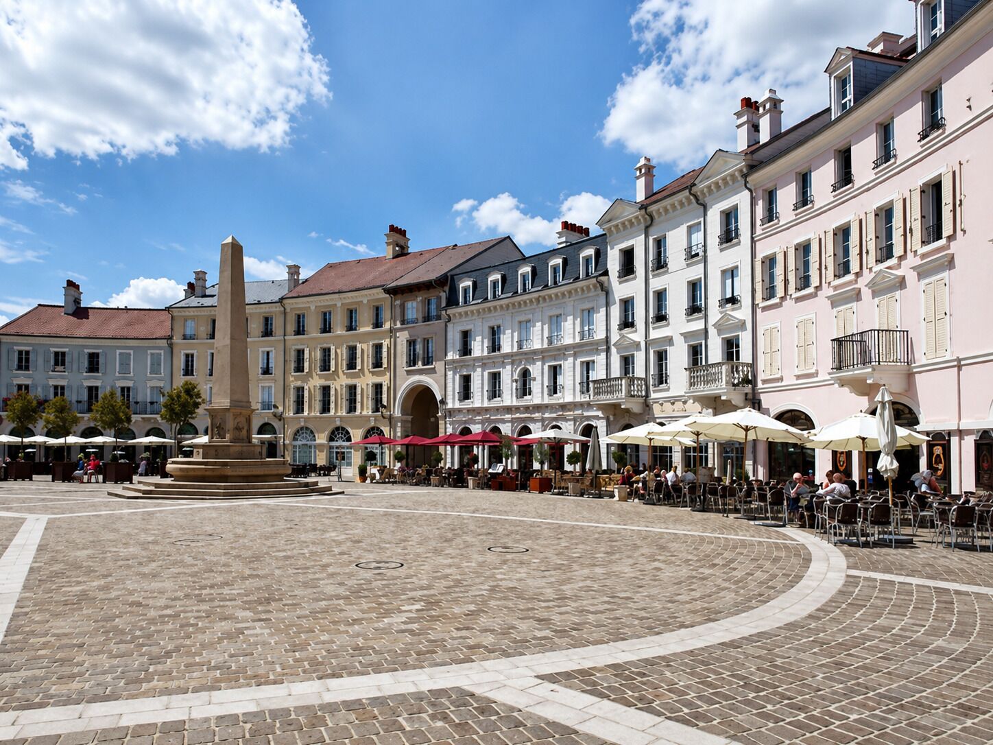 Une place historique pavée de pierres, ornée d’un monument central et présentant une architecture européenne traditionnelle.