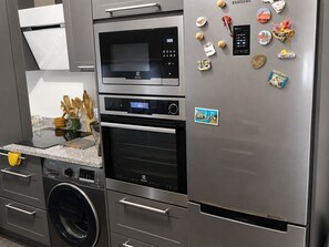 Una cocina con un refrigerador, horno y microondas de acero inoxidable. Hay imanes y un pequeño refrigerador en la puerta.