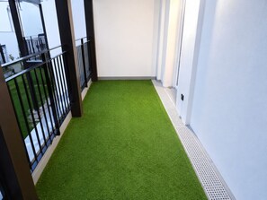 A narrow corridor with artificial green flooring, white walls, and a black metal railing on one side.