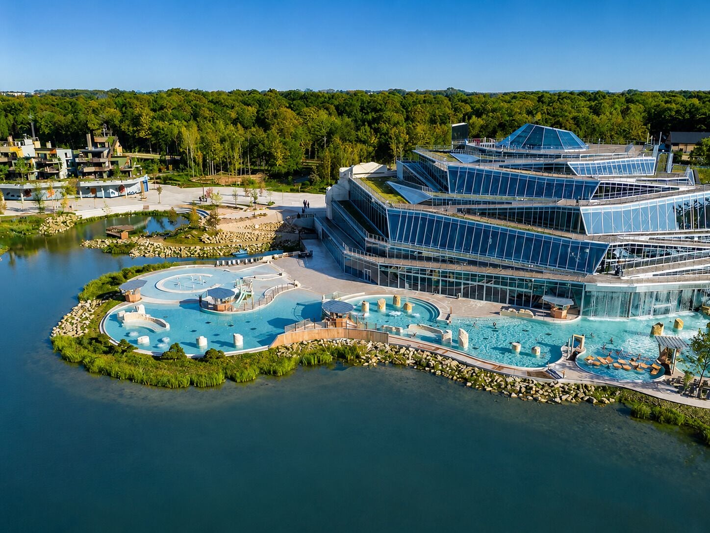 Un hôtel moderne doté d’un grand espace piscine, comprenant un jacuzzi et un toboggan aquatique.