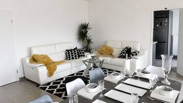Un salon moderne comprenant un coin repas, des canapés blancs, une table basse en verre et un tapis aux motifs noir et blanc.