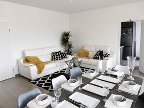 A modern living room with a dining area, white sofas, a glass coffee table, and a black and white patterned rug. - Beautiful 110 m² Villa & Large Garden – 5 Min from Disneyland Paris (Serris)