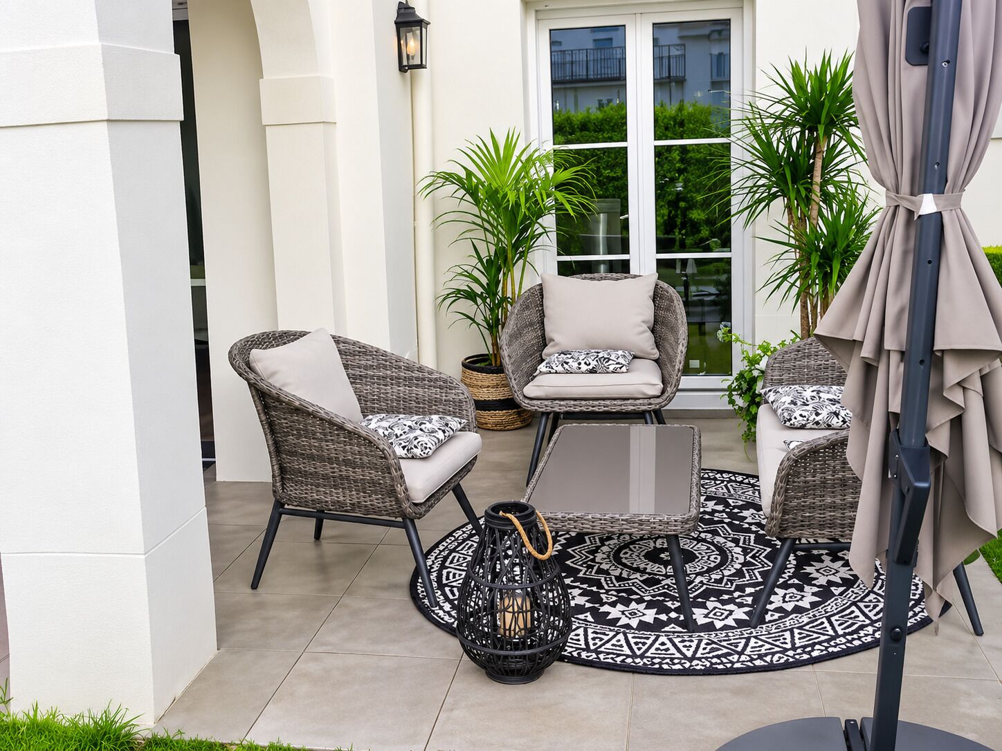 A patio with wicker furniture, a patterned rug, and a potted plant.