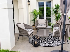 A patio with wicker furniture, a patterned rug, and a potted plant.