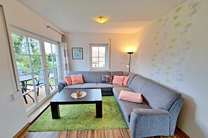 A living room with a grey sofa, a black coffee table, and a green rug. There are windows and a lamp. - Tinnemeyer holiday apartment (Heringsdorf (Seebad))
