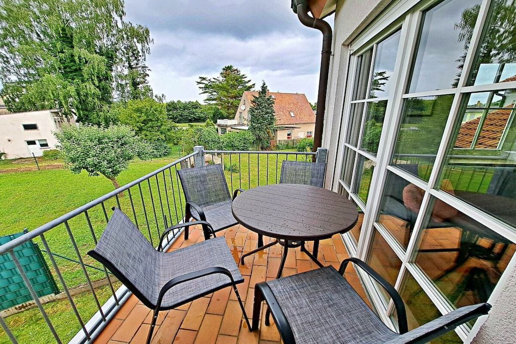 A balcony with a round table and four chairs, surrounded by a metal railing.