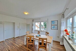 Ein geräumiger Raum mit einem Holztisch, Stühlen, einem Heizkörper und großen Fenstern.