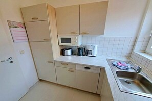 Eine kompakte Küche mit Mikrowelle, Toaster und Kaffeemaschine auf der Arbeitsplatte, einem Geschirrspüler und einem Spülbecken mit Fenster darüber.