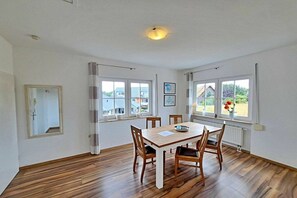 A dining room with a wooden table and chairs, large windows with curtains, and a view of the outside. - Tinnemeyer holiday apartment (Heringsdorf (Seebad))