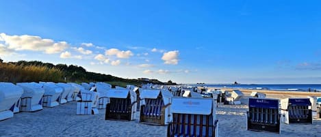 Beach huts arranged in rows on a sandy beach with a clear sky.