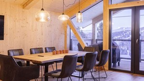 A wooden interior with a large table and chairs, large windows, and a view of a snowy landscape. - Superior Chalet # 2 with Sauna & Hot Tub (Turrach)