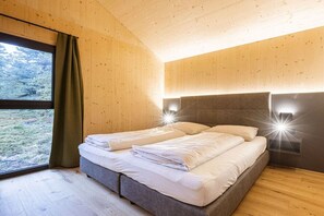 A bedroom with a double bed, wooden walls, a large window with curtains, and wall-mounted lights. - Superior Chalet # 2 with Sauna & Hot Tub (Turrach)