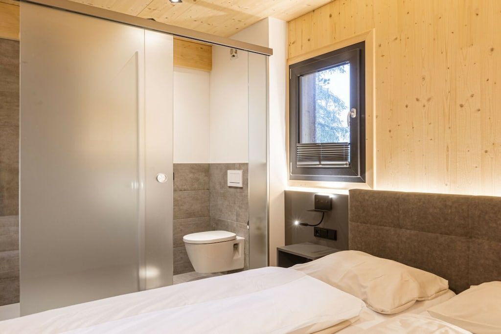 A modern bedroom with a bed, a window, and a separate toilet area.