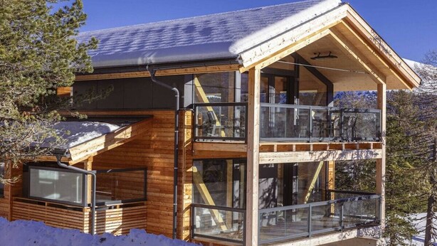 A wooden cabin with a balcony and large windows, surrounded by snow. - Superior Chalet # 2 with Sauna & Hot Tub (Turrach)