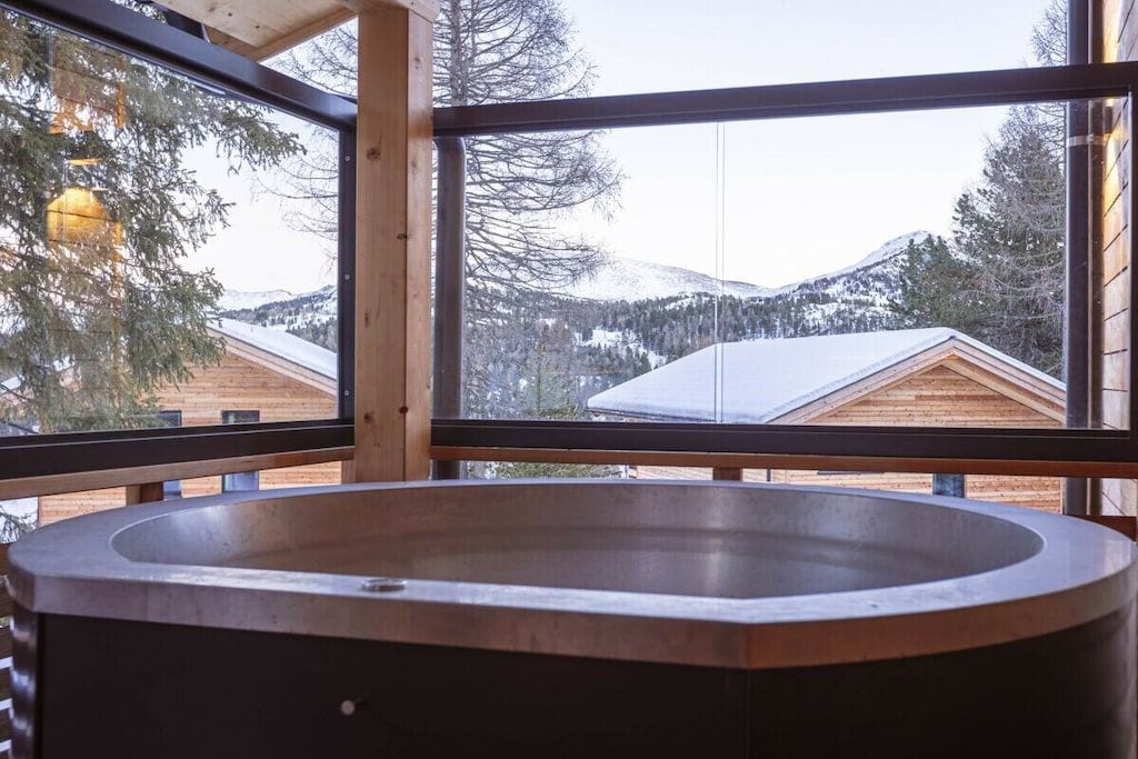 A spa area with a large, empty bathtub and a view of snow-covered mountains through large windows.