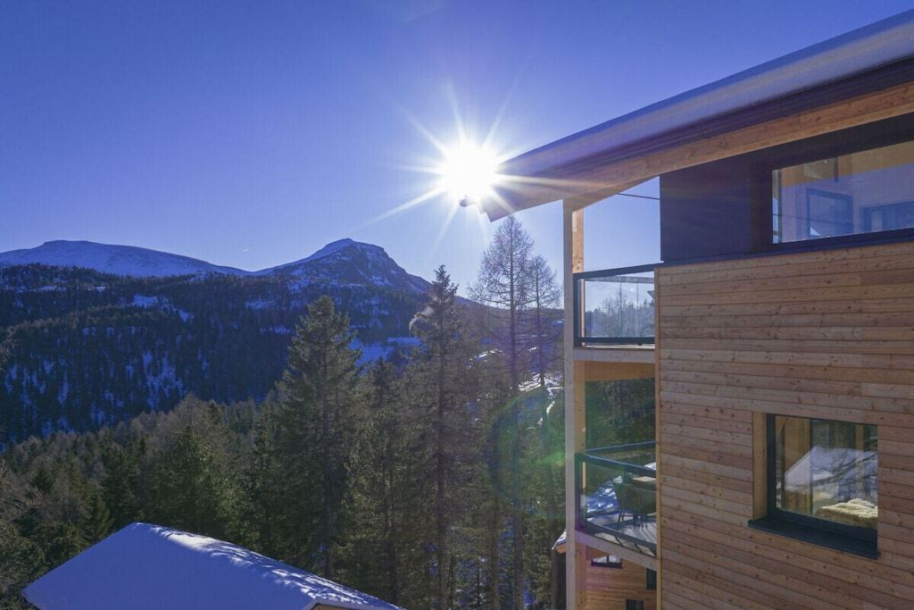 A modern building with a wooden exterior and large windows, overlooking a mountainous landscape.