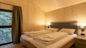 Quarto com painéis de madeira, cama, luminárias de cabeceira e janela com cortinas.