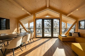 Un interior moderno con zona de comedor, asientos y amplios ventanales que ofrecen vistas a árboles cubiertos de nieve.