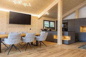 Moderni sisustus, jossa on ruokailutila, keittiö ja suuri, seinälle asennettu taulutelevisio.