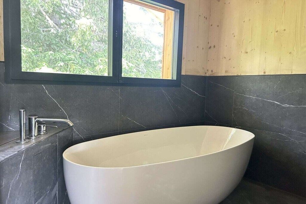 A modern bathroom with a freestanding bathtub, a window, and dark marble walls.