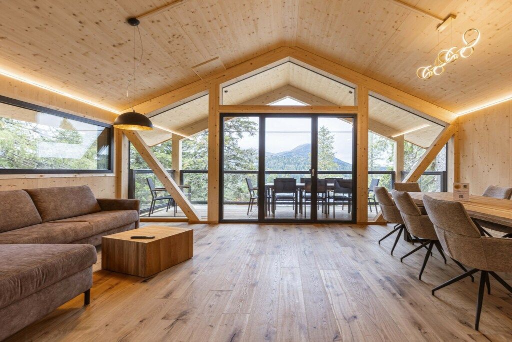A spacious room with a high ceiling, wooden beams, a large table with chairs, and a sofa.