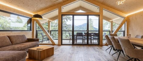 A spacious room with a high ceiling, wooden beams, a large table with chairs, and a sofa.