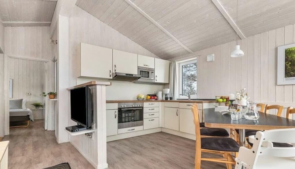 A modern kitchen with white cabinetry, a built-in oven, and a dining area with a table and chairs.