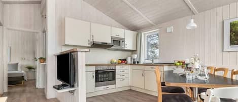 A modern kitchen with white cabinetry, a built-in oven, and a dining area with a table and chairs.