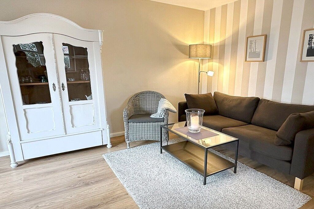Ein Wohnzimmer mit einem weißen Schrank, einem Korbstuhl, einem braunen Sofa, einem Glastisch und einer Stehlampe.