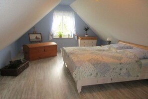 Ein Schlafzimmer mit einem Bett, einem Schminktisch, einem Nachttisch und einem Fenster mit Vorhängen.
