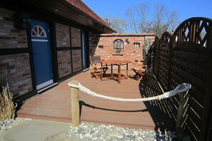 Een terras met een houten tafel en stoelen, een blauwe deur en een bakstenen muur met decoratieve details.
