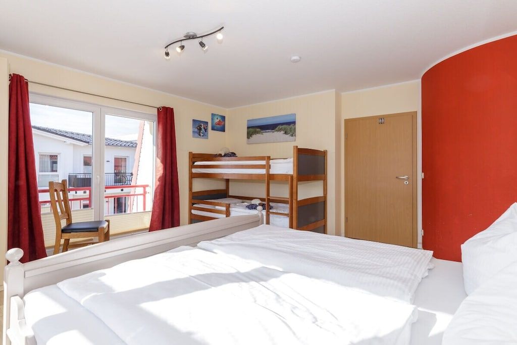 Een hotelkamer met een bed, stapelbedden, een raam met gordijnen, een deur en een klein tafeltje met een stoel.