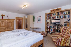 A bedroom with a bed, a bedside table, a bookshelf, and a television. - Dune Garden Kühlungsborn (Kühlungsborn)