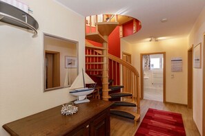 Una escalera con barandilla de madera y detalles rojos, que conduce a un rellano con alfombra roja y una pequeña mesa con un adorno.