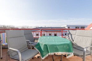 A terrace with two chairs and a table, a red railing, and a building with a tiled roof in the background. - Dune Garden Kühlungsborn (Kühlungsborn)