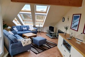 A modern living room with a sectional sofa, a coffee table, and a TV. There are skylights providing natural light. - Dune Garden Kühlungsborn (Kühlungsborn)