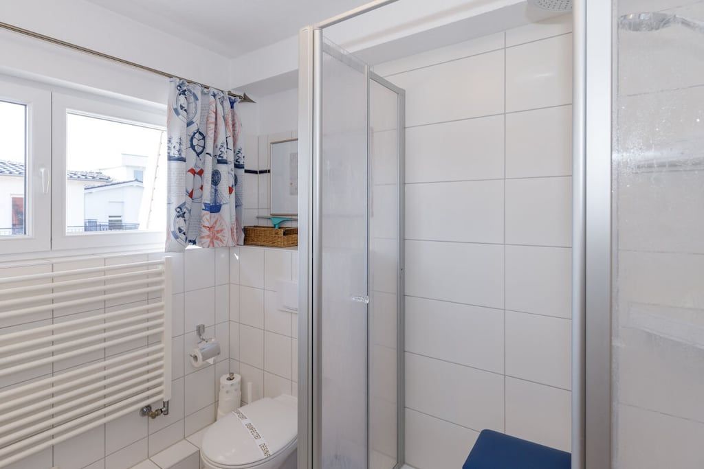 Een badkamer met toilet, douchecabine en raam met gordijn.