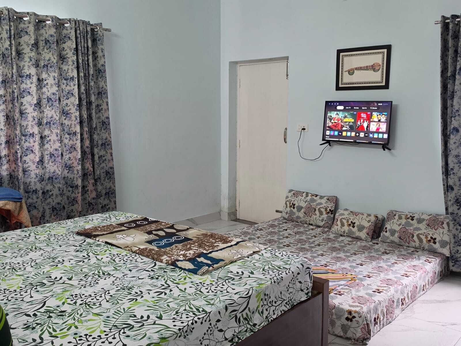 A bedroom with a bed, a sofa, a television mounted on the wall, and a door.