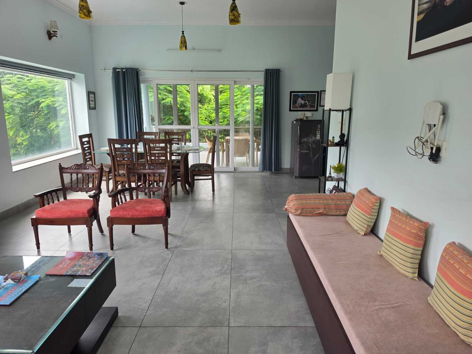 A spacious living area with a sofa, chairs, a dining table, and a view through large windows.